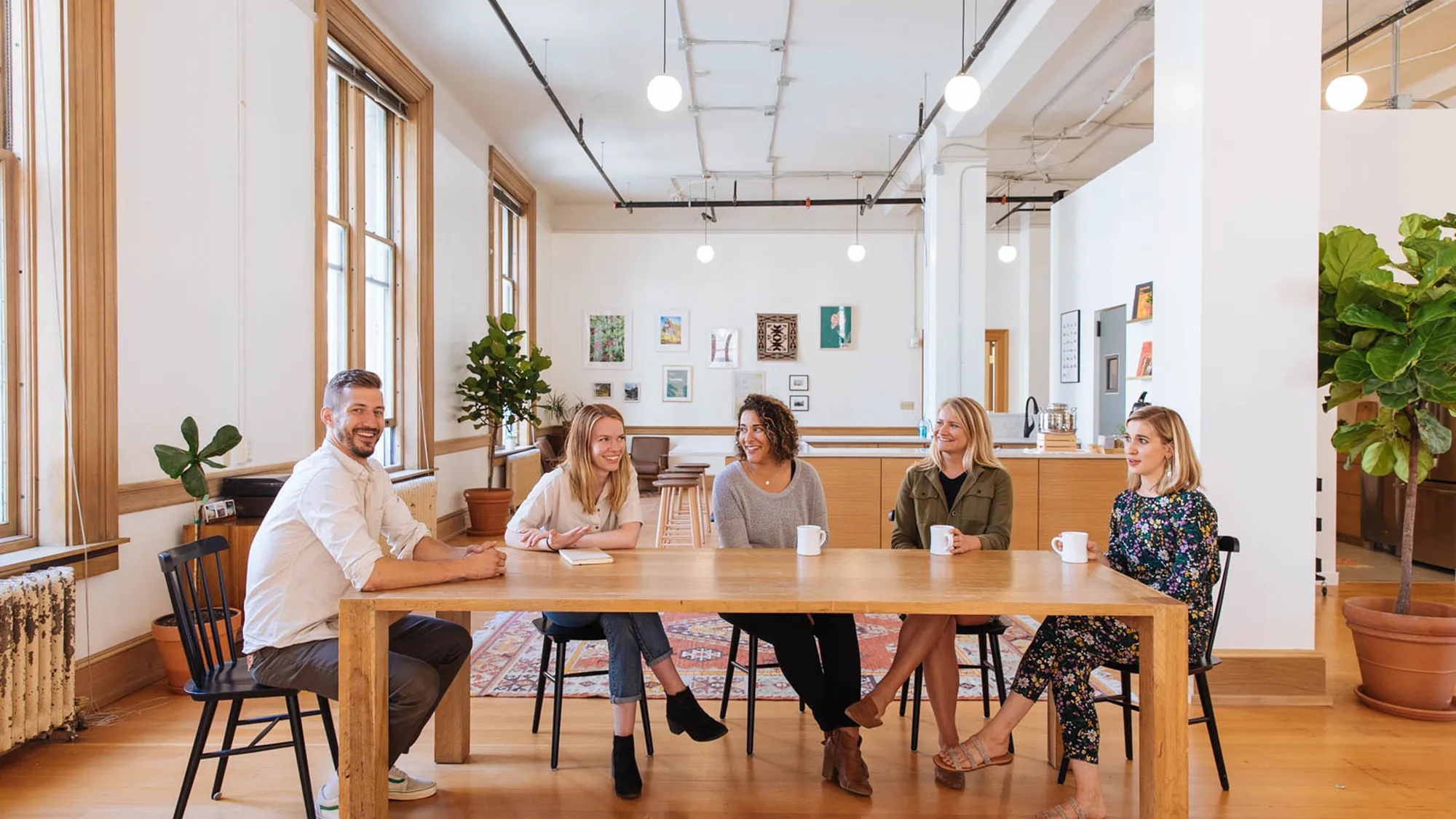 5 smiling people sitting at a table drinking coffee in a workspace