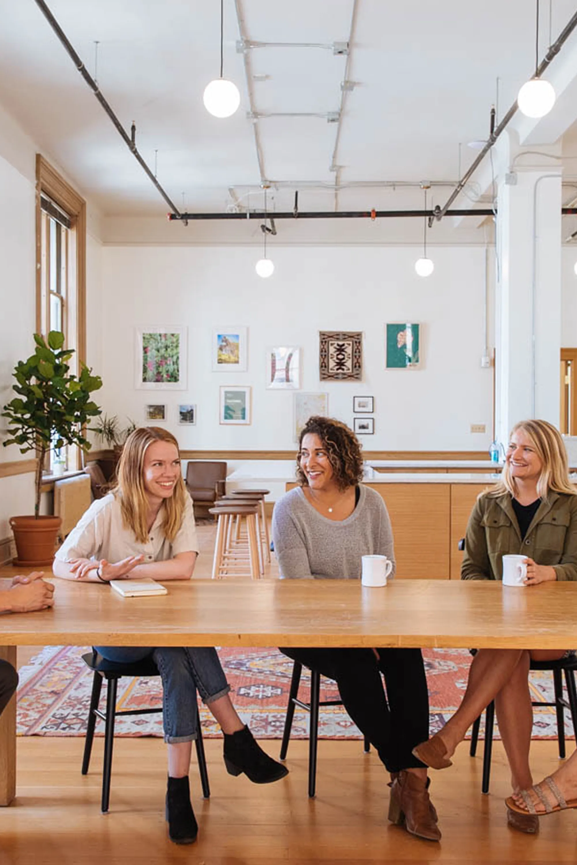 5 smiling people sitting at a table drinking coffee in a workspace