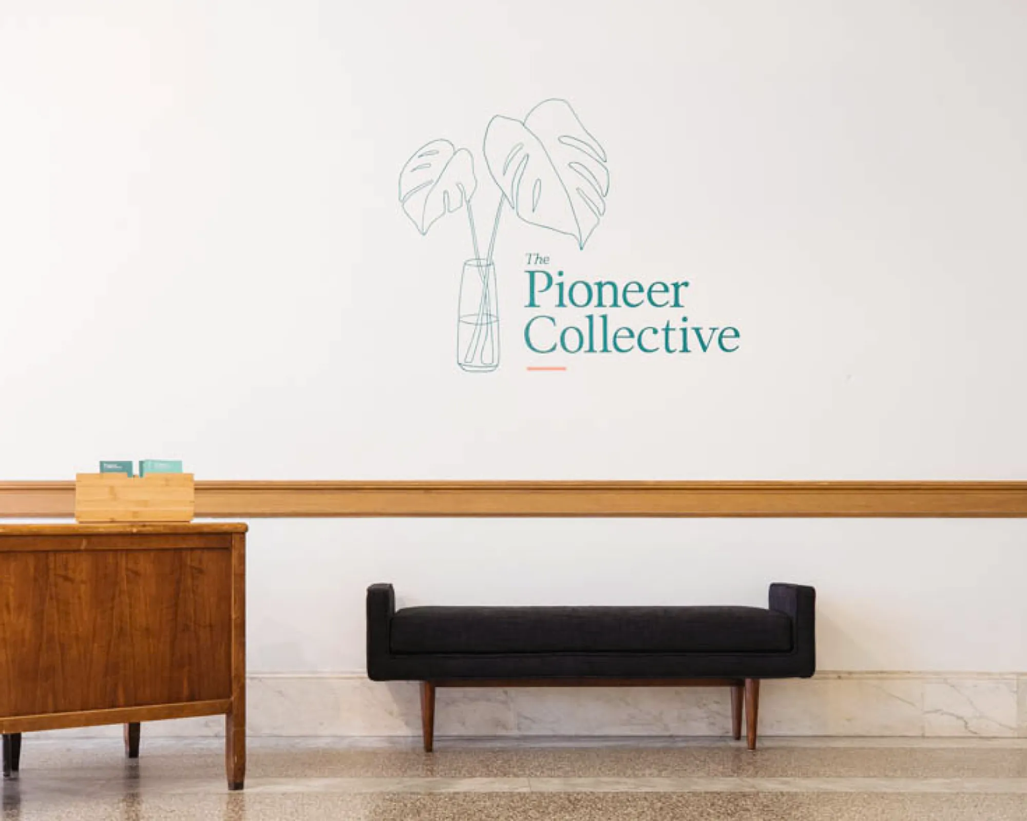 Black bench and wooden dresser with the Pioneer Collective logo on the back wall